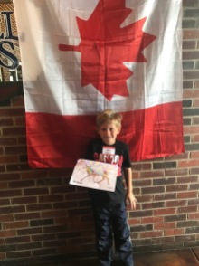 Young winner of drawing contest posing with his drawing in front of Canada flag